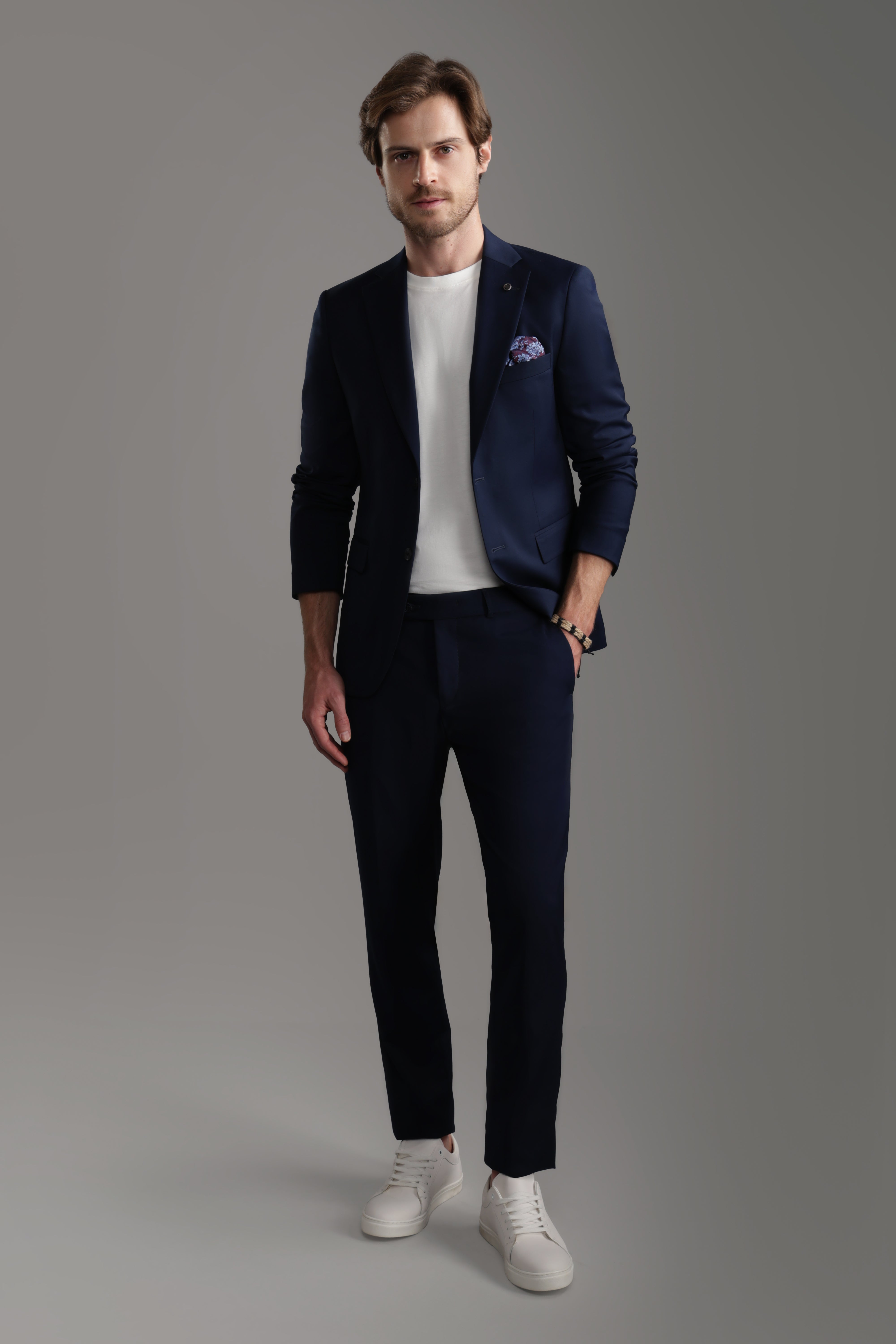 Man wearing a navy suit with a white t-shirt and sneakers, showcasing a modern, casual look for formal occasions.
