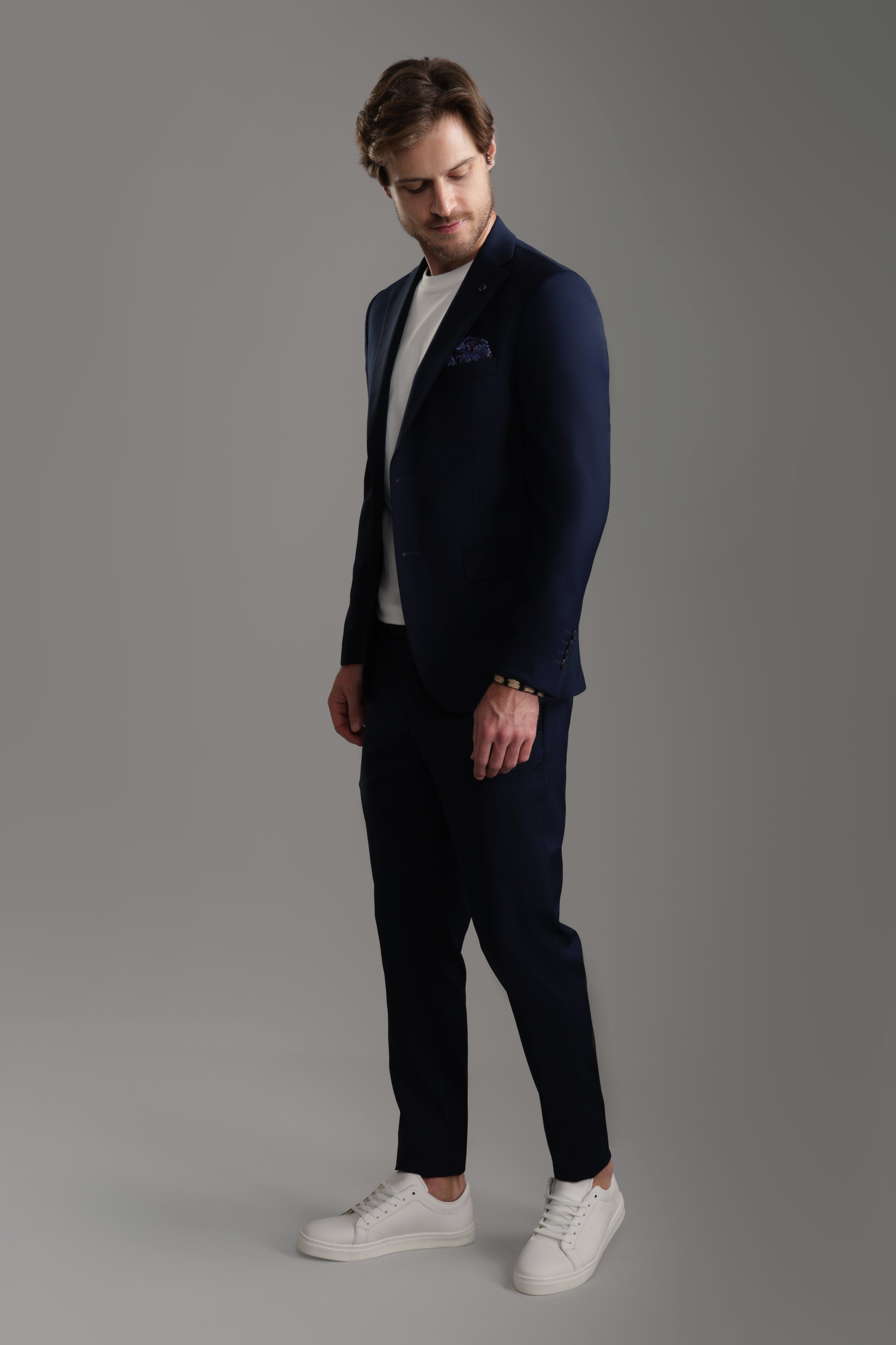 Navy suit with tailored pants and jacket, styled with a casual shirt and sneakers, perfect for formal occasions.