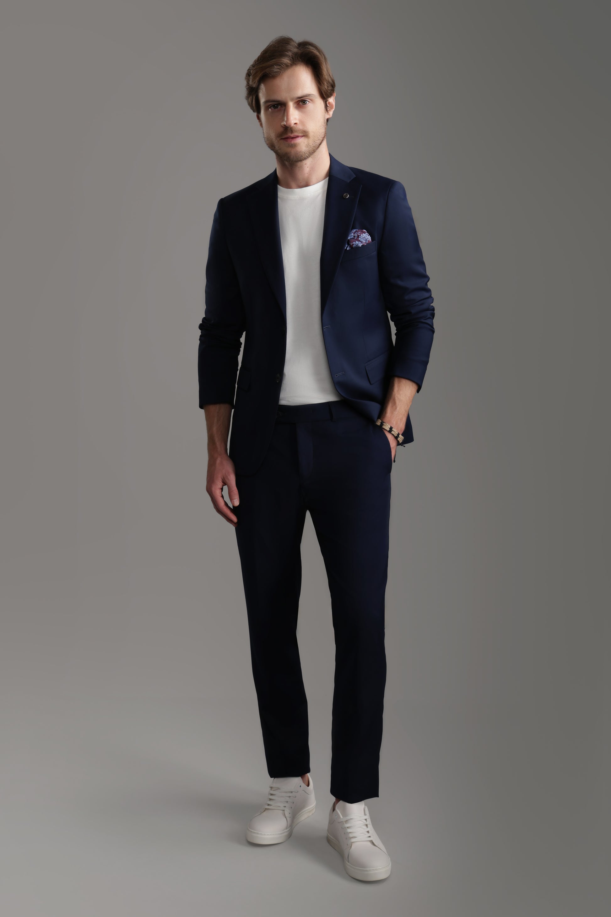 Man wearing a navy suit with a white t-shirt and sneakers, showcasing a modern, casual look for formal occasions.